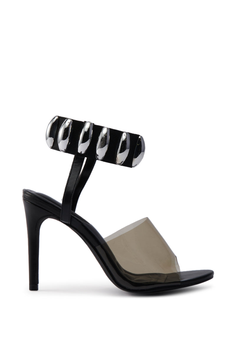 The AKIRA MADRIDI BLACK PVC AND METAL SANDAL is a chic black stiletto with a transparent front strap and an ankle strap embellished with large, shiny silver metal oval accents. 3