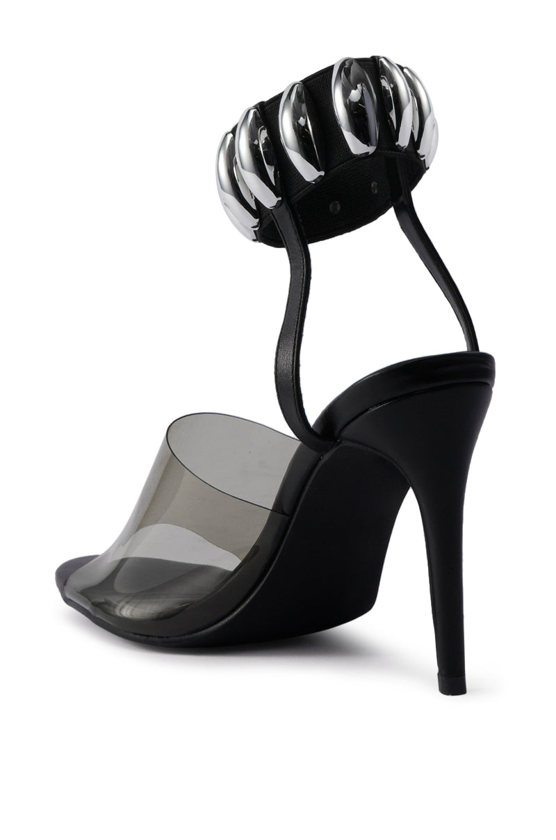 The AKIRA MADRIDI BLACK PVC AND METAL SANDAL is a black stiletto heel with a transparent toe strap and a metal-accented ankle strap decorated with large, shiny ovals for a bold, modern style. 5