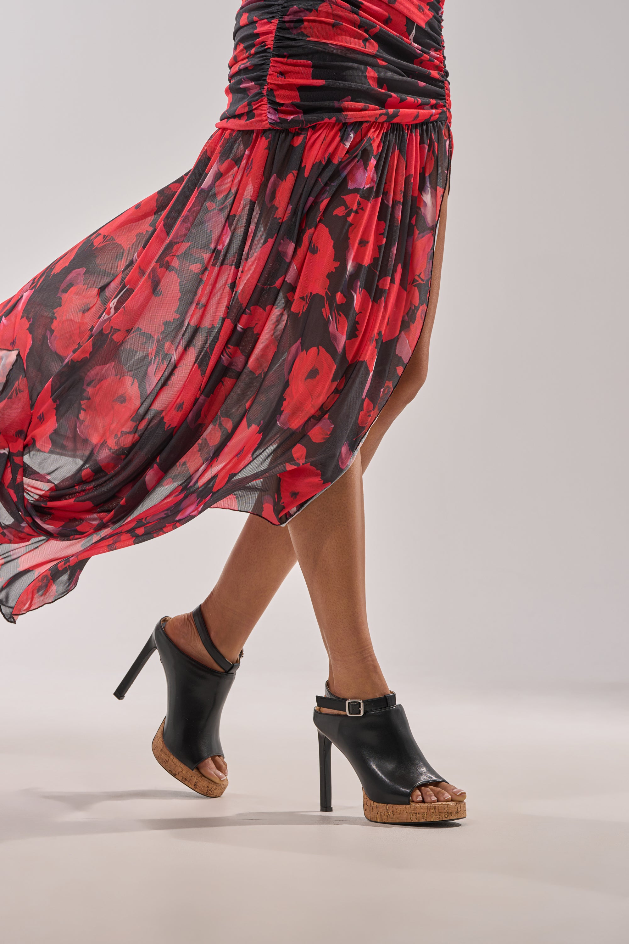 A person strides forward in a flowing red and black floral dress, showcasing the dress’s slit and movement while wearing AZALEA WANG MAELIE BLACK AND CORK STILETTO SANDALS. 1