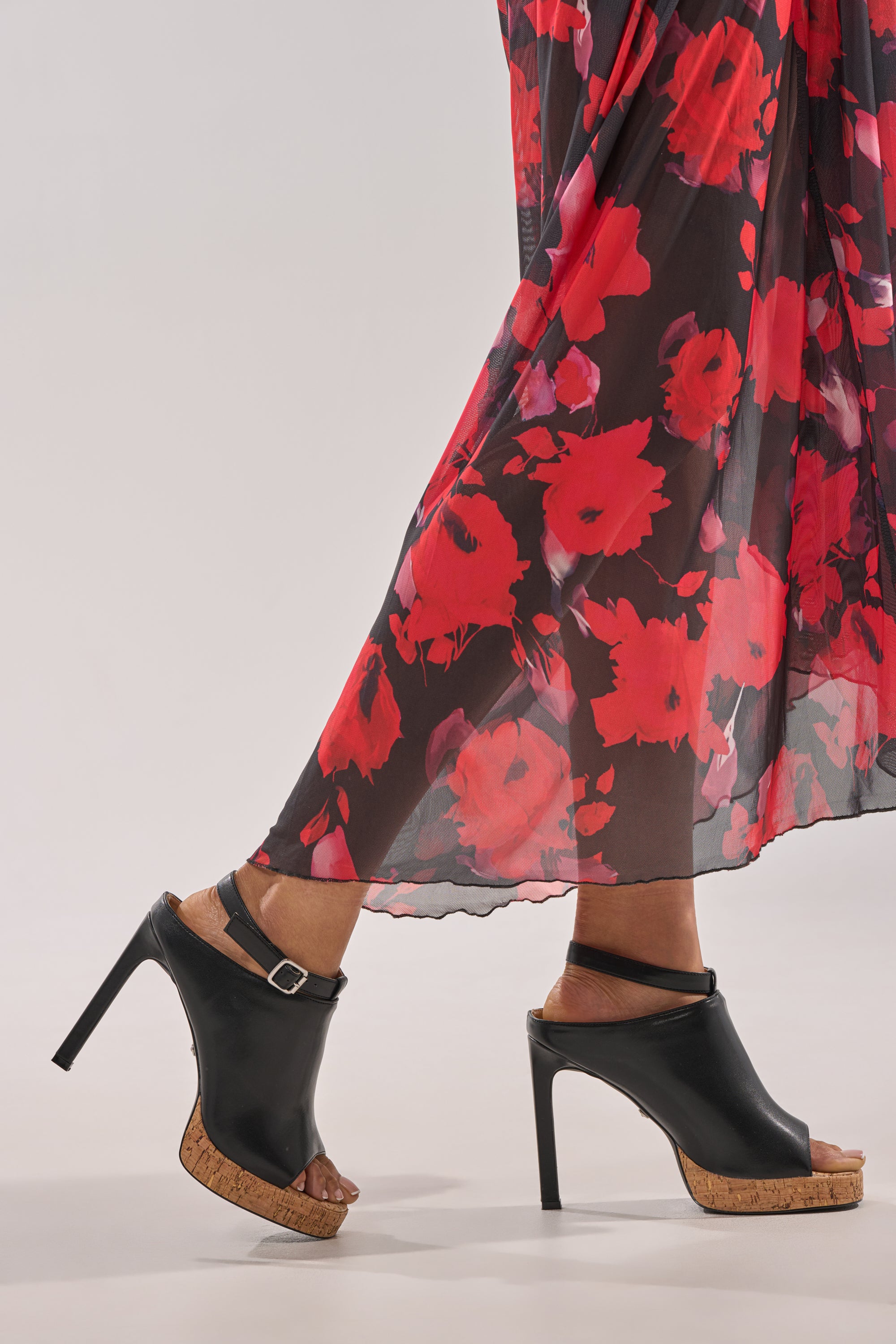 A person wears a flowing, sheer black and red floral skirt paired with AZALEA WANG MAELIE BLACK AND CORK STILETTO SANDALS. The image highlights the lower legs and feet against a plain background. 2