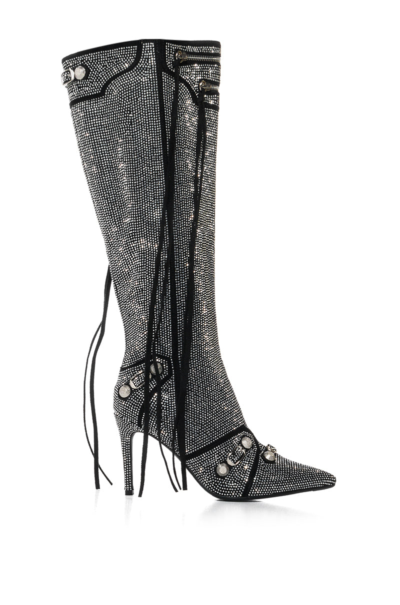 The AZALEA WANG MAEVE SILVER STILETTO BOOT is a knee-high, pointed-toe boot adorned with sparkling rhinestones and decorative laces, featuring silver studs and a stiletto heel.