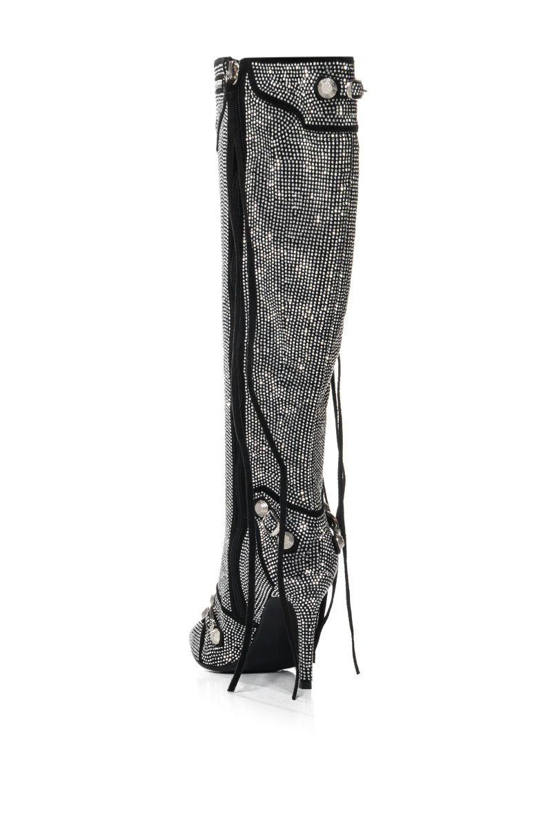 The AZALEA WANG MAEVE SILVER STILETTO BOOT showcases rhinestone embellishments that elegantly complement a stiletto heel, set against a white background and adorned with decorative buckles and black laces along its knee-height shaft.