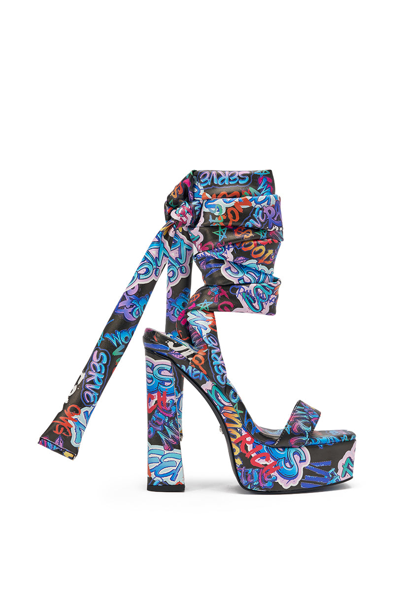 The AKIRA GOLD MAGRITTE GRAFFITI STRAPPY CHUNKY SANDAL boasts vibrant patterns, an open toe, long ankle wrap straps, and a block heel—all in bold graffiti. Ideal for standout streetwear looks. 3