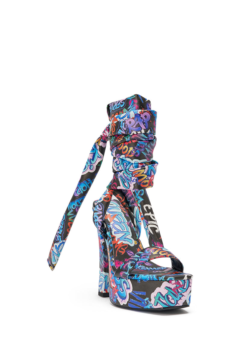 The AKIRA GOLD MAGRITTE GRAFFITI STRAPPY CHUNKY SANDAL features ankle wrap straps and bold graffiti-style text and patterns on a black background, making it the perfect statement piece for streetwear looks. 4