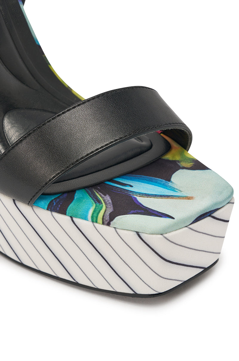 The AKIRA GOLD MAGRITTE Multi Stripe Print Chunky Platform Sandal features black leather straps, a floral abstract-print insole, and a thick white sole with bold diagonal black stripes. 7