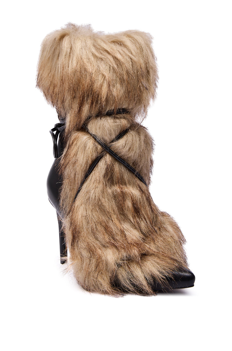 The AZALEA WANG MAHTAMA BLACK FUR EMBELLISHED BOOTIE is a high-heeled bootie with a pointed toe, shaggy light brown faux fur overlay, and crisscrossing black leather straps elegantly wrapping the ankle and foot.