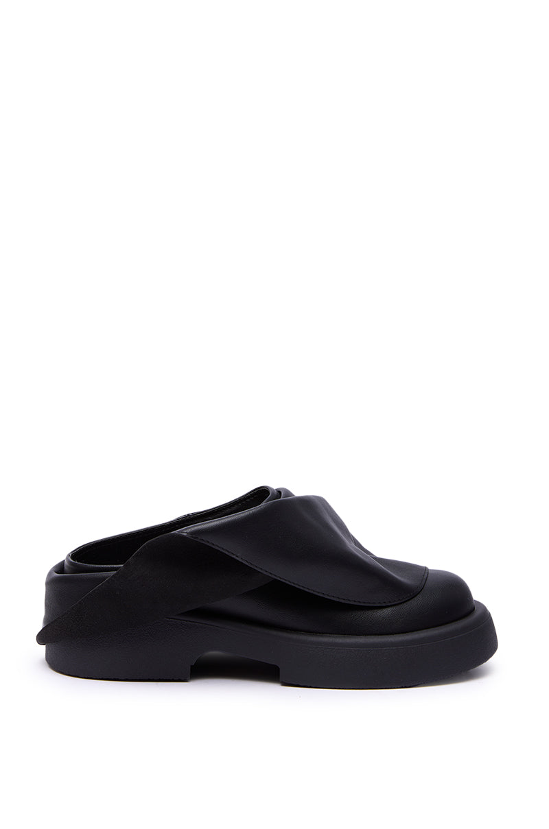 The AZALEA WANG MAITYE BLACK RUCHED FLAT is a faux leather slip-on featuring a chunky flat sole and overlapping wide straps, shown in black against a white background.