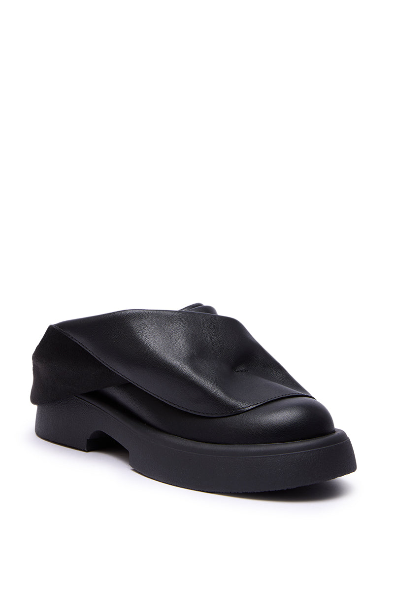 The AZALEA WANG MAITYE BLACK RUCHED FLAT features a chunky sole and an eye-catching folded faux leather upper that drapes over the top, creating a distinctive and modern look.