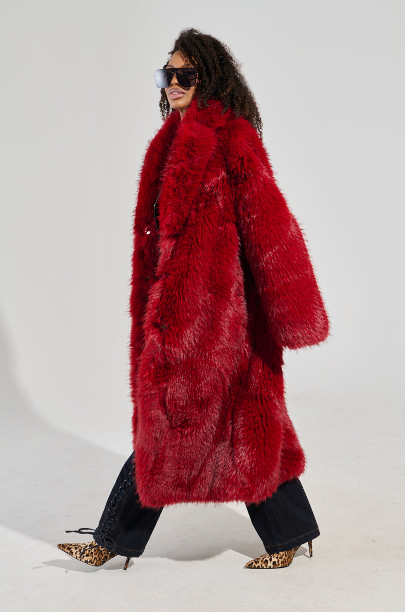 A person exudes an air of sophistication in the MAJOUR FUR COAT, confidently walking with their curly hair and chic sunglasses enhancing the ensemble. The leopard print heels and black pants provide a striking contrast against a plain white background, perfectly showcasing the essence of luxurious outerwear fashion.