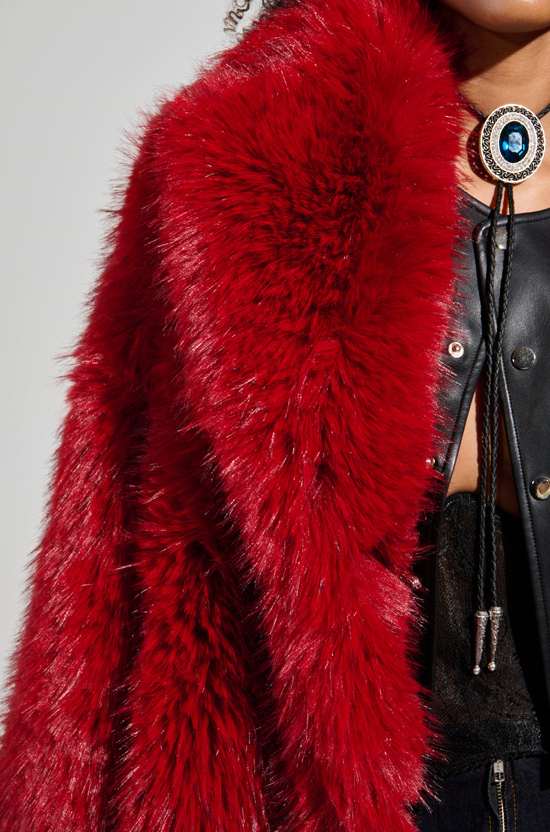 Close-up of a person wearing the luxurious MAJOUR FUR COAT in vibrant red faux fur, paired with a black outfit. A bolo tie with a round blue stone clasp accents the look, adding a sophisticated finish to the ensemble.