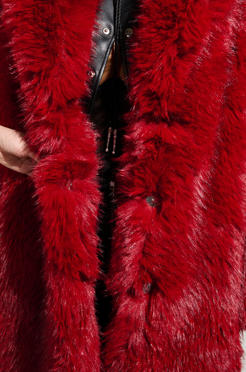 Close-up of a person wearing the MAJOUR FUR COAT by AKIRA Label in vibrant red, featuring a sleek black inner lining. This luxurious outerwear showcases glossy fur and elegant black buttons along the front. A hand is subtly visible, gently holding the coat open.