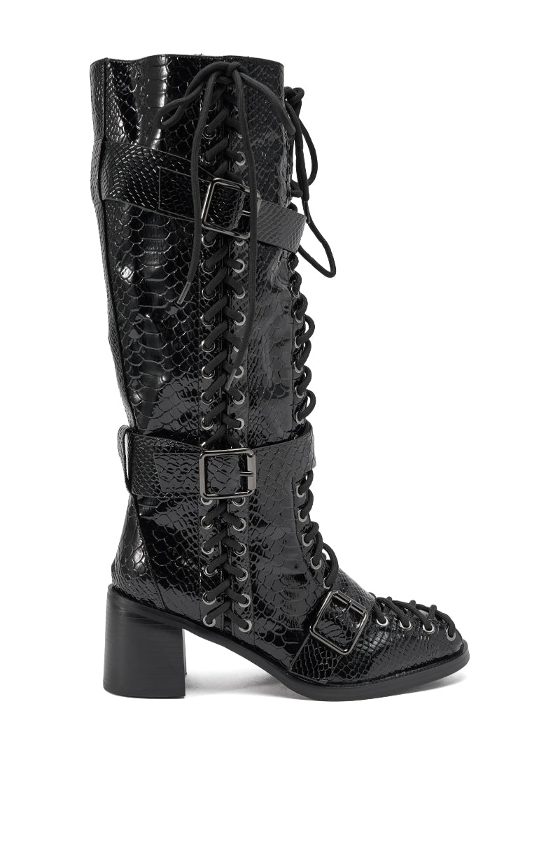 The AZALEA WANG MAKAR BLACK CROC LACE UP DETAIL BOOT is a knee-high, black croc boot with a block heel, side buckles, and a shiny snakeskin texture that brings edgy style to any outfit.