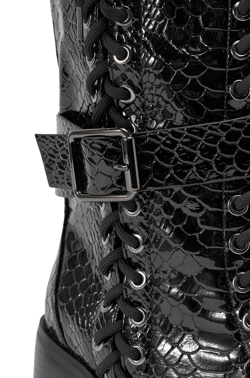 Close-up of the AZALEA WANG MAKAR BLACK CROC LACE UP DETAIL BOOT, featuring shiny black croc texture, black laces threaded through metal eyelets, and a decorative strap with a silver buckle.