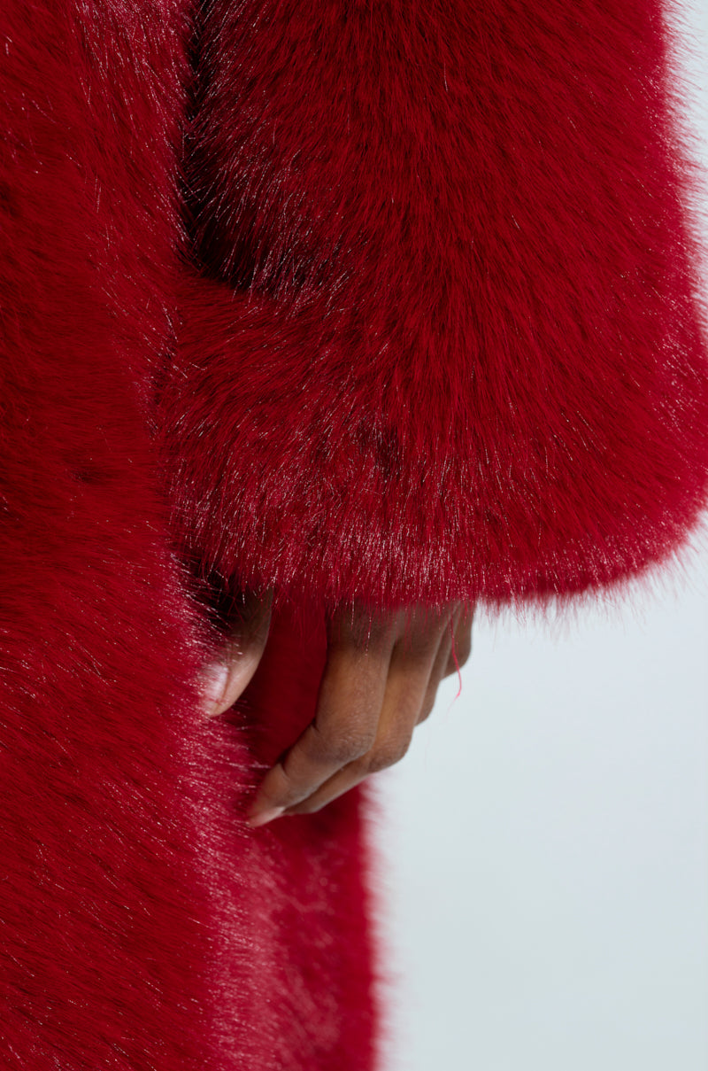 A close-up captures a person wearing the vibrant MANCHESTER HOODED FAUX FUR IN WINE. The image focuses on the sleeve and hand, emphasizing the garment's rich texture and color against a light background.