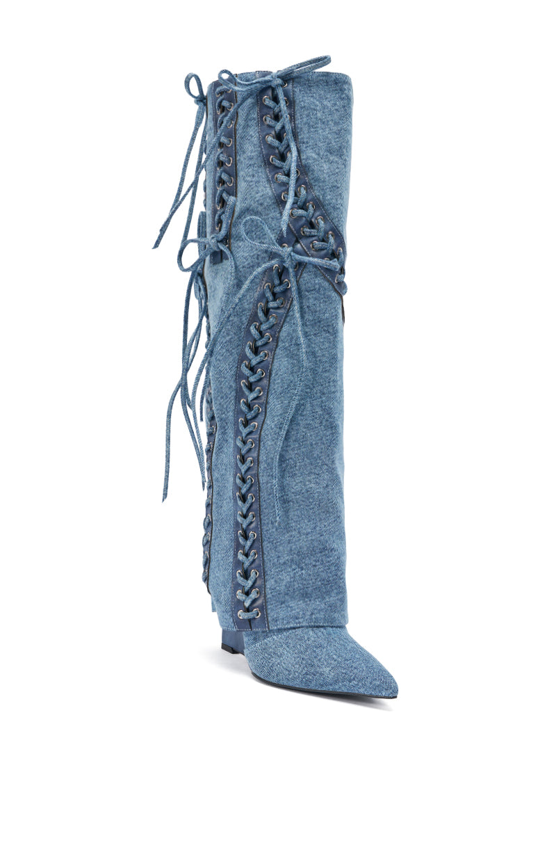 The AKIRA GOLD MANTIGNA DENIM WEDGE BOOT is a tall, pointed-toe denim boot with decorative corset lacing up the front and sides, plus extra long laces tied at the top and sides.