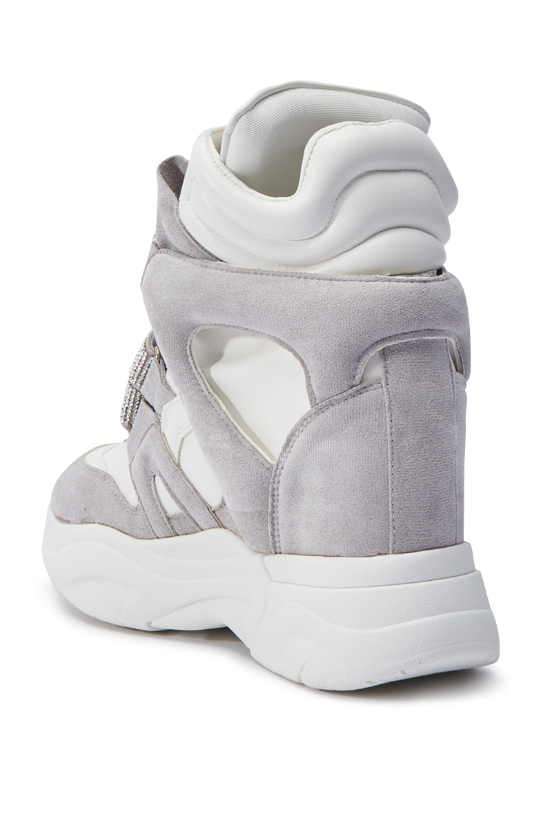 Introducing the MARANTO WHITE WEDGE SNEAKER, a fashionable high-top crafted with a blend of faux suede and faux leather. This sneaker boasts a chunky white sole, intricate cutout details, and a rhinestone-embellished Velcro foot strap for a contemporary sporty aesthetic.