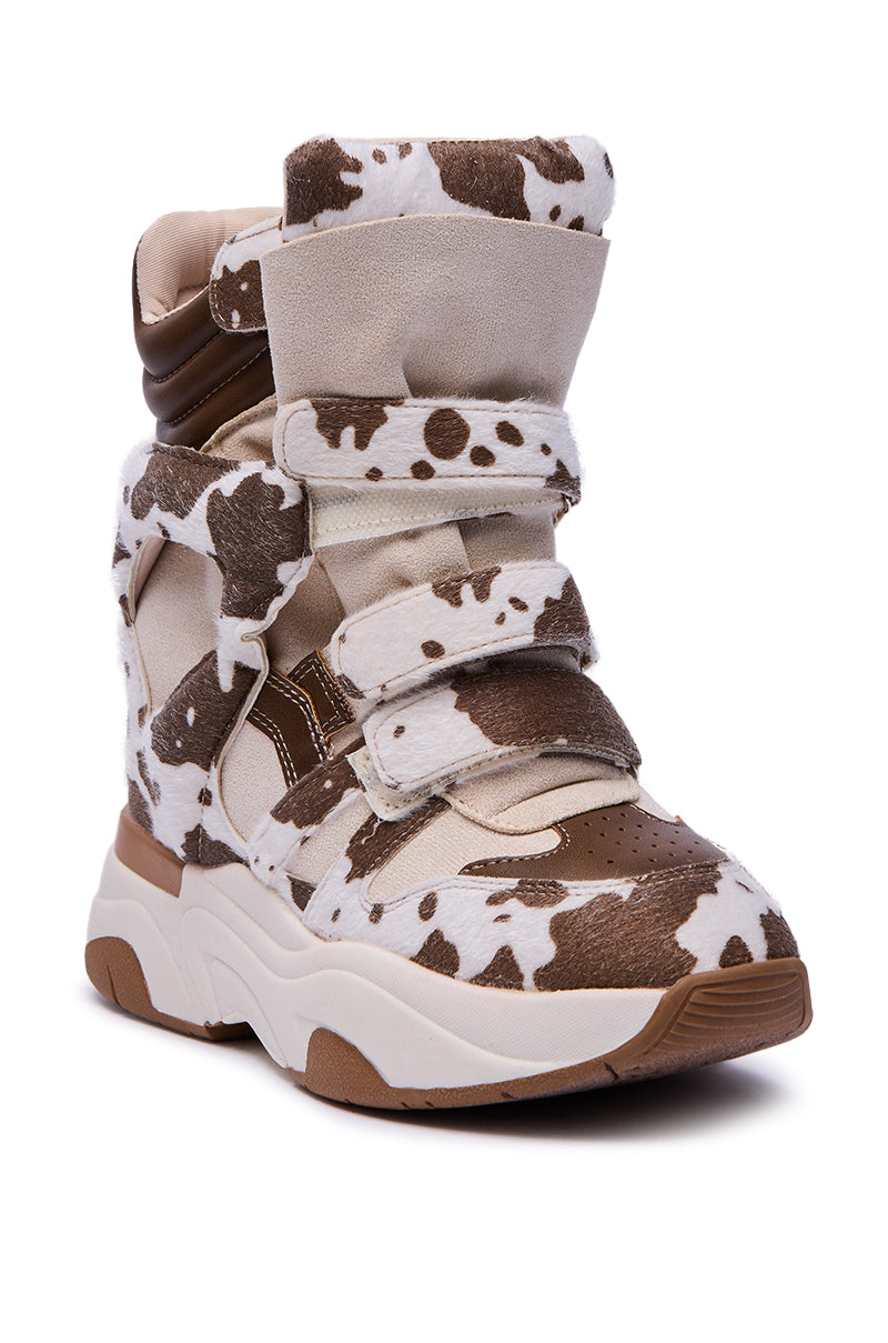 The MARANTO COW COLOR BLOCKED WEDGE SNEAKER is a high-top with chunky soles, beige straps, padded ankle details, a hidden wedge heel, and a stylish brown-and-white cow print color-blocked design.