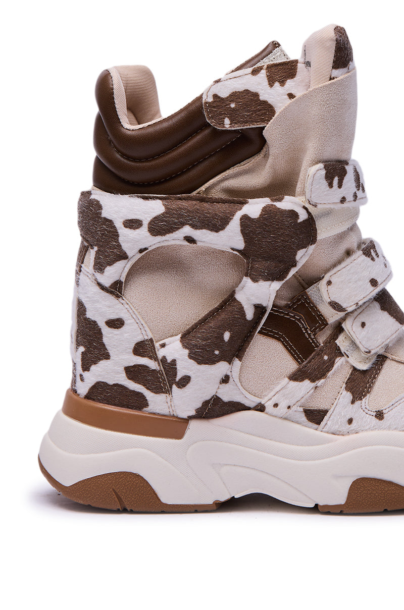 The MARANTO COW COLOR BLOCKED WEDGE SNEAKER is a high-top with a cow print, chunky wedge sole, multiple Velcro straps, and cushioned ankle support—offering bold style and all-day comfort.