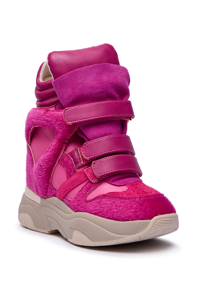 The MARANTO FUCHSIA COLOR BLOCKED WEDGE SNEAKER features a chunky sole, vibrant pink color-block design, suede and faux fur textures, thick Velcro straps, and layered ankle padding for style and comfort.