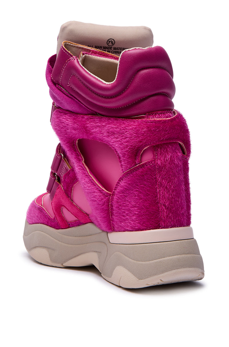 The MARANTO FUCHSIA COLOR BLOCKED WEDGE SNEAKER is a bright pink sneaker with faux fur, shiny accents, cut-out details, thick padded collar, hidden wedge heel, and chunky white sole shown from the back angle.