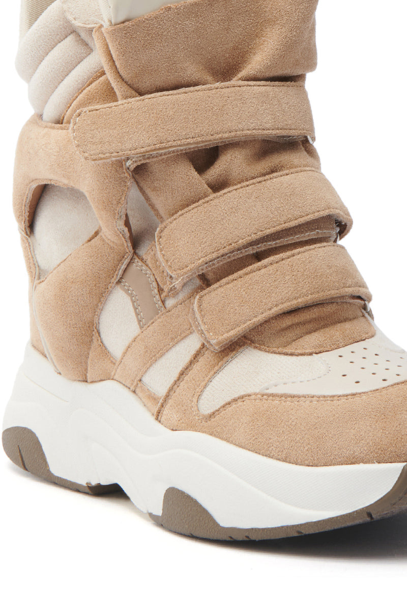 Close-up of the MARANTO TAUPE WEDGE SNEAKER showcasing adjustable straps on a tan suede design, cut-out details, a chunky white sole, and a hidden wedge heel for added height in a retro sporty style.