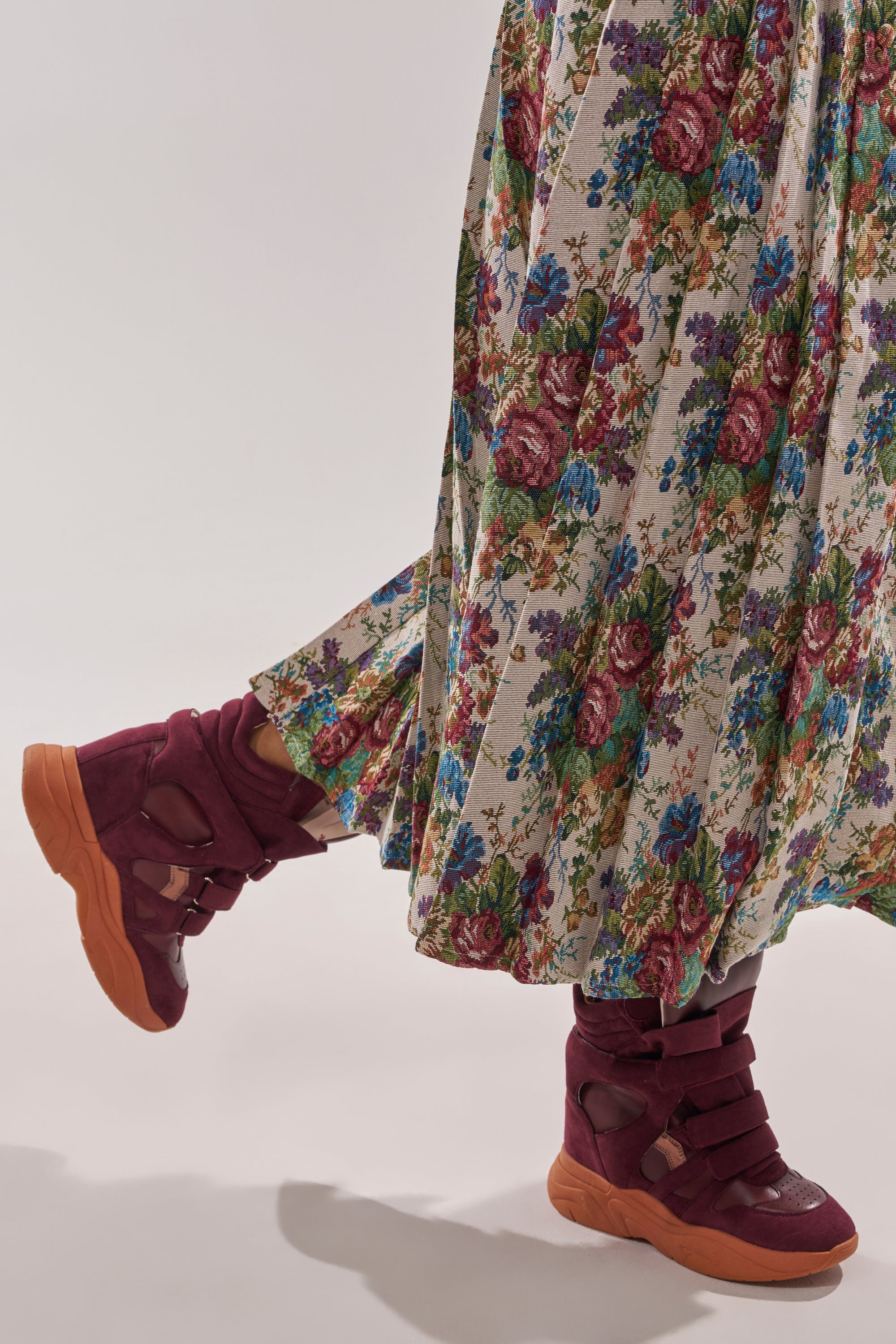 A person wearing a long, floral-patterned skirt and MARANTO BURGUNDY WEDGE FAUX SUEDE SNEAKER with thick orange soles stands against a plain background. 4