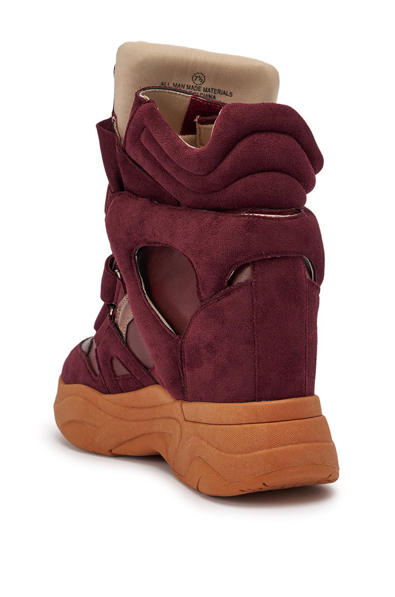 The MARANTO BURGUNDY WEDGE FAUX SUEDE SNEAKER is a maroon high-top with cut-out details, cushioned tan collar, and thick tan rubber sole featuring a concealed wedge heel, shown from the rear on a white background. 7