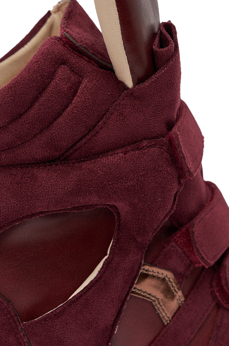 Close-up of the MARANTO BURGUNDY WEDGE FAUX SUEDE SNEAKER, showcasing detailed stitching, textured suede and leather layers, cutout accents, a strap, padded high-top upper, and a peek of the inner lining. 8