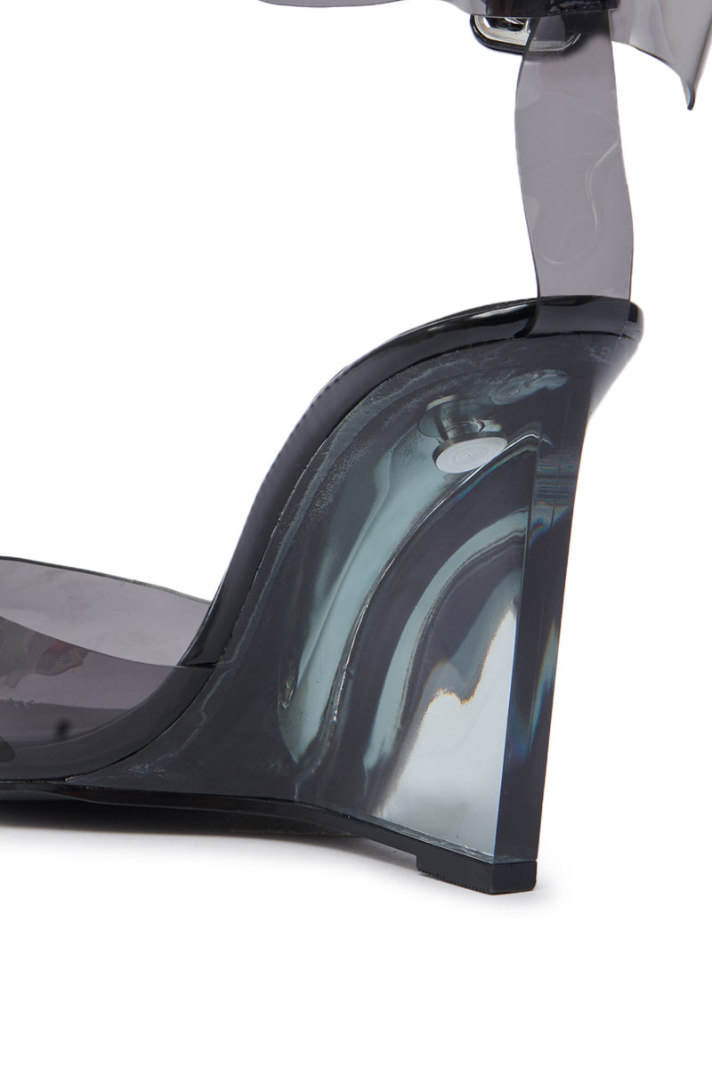 Close-up of the AZALEA WANG MARCO SMOKE PVC PUMP, featuring a pointed toe, transparent smoky grey wedge heel and strap, with shiny, reflective material. 8