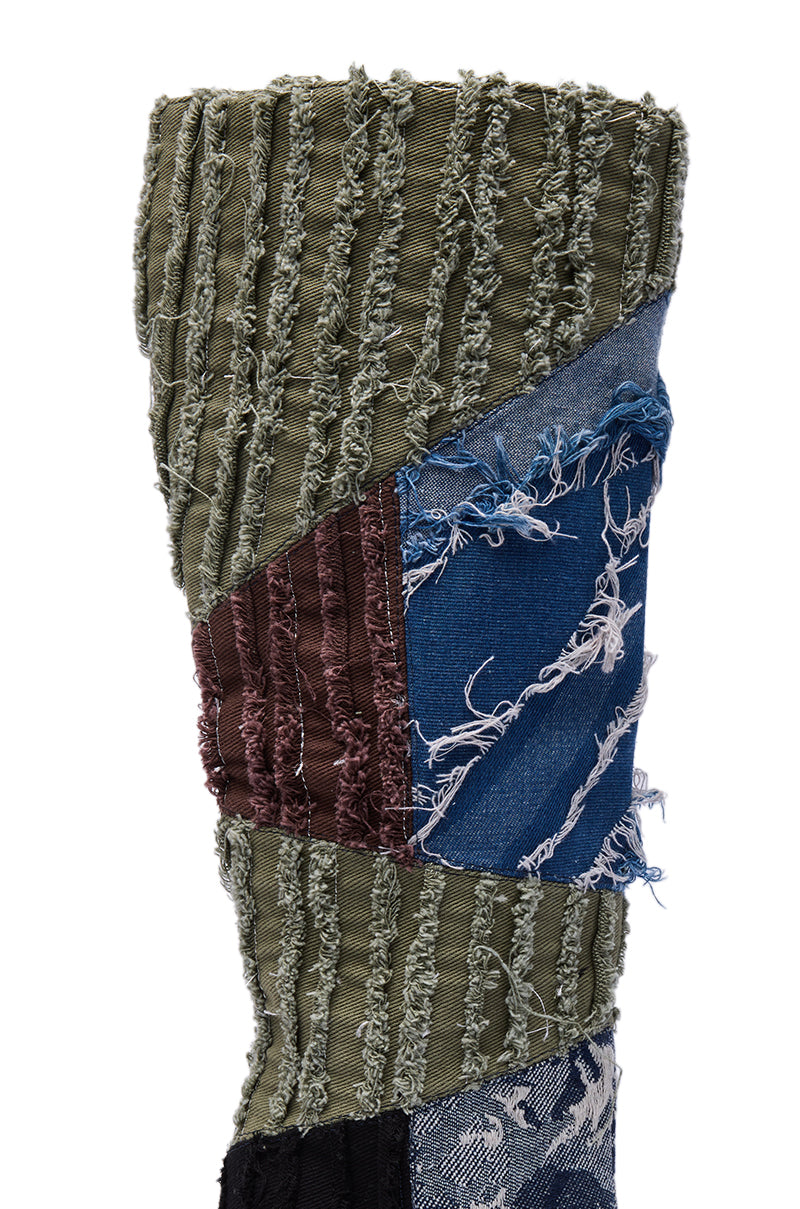 A close-up of a textile patchwork with frayed green, brown, and blue denim, visible stitching, and textured edges—reflecting the rugged style of the AZALEA WANG MARGEE MULTI CHUNKY KNEE HIGH BOOT.