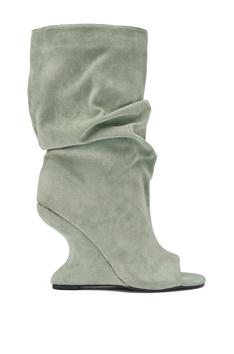 The AZALEA WANG MARIN SAGE FAUX SUEDE WEDGE BOOTIE is a light sage green slouchy bootie with a sculptural curved wedge heel and open toe, displayed in profile against a white background. 4