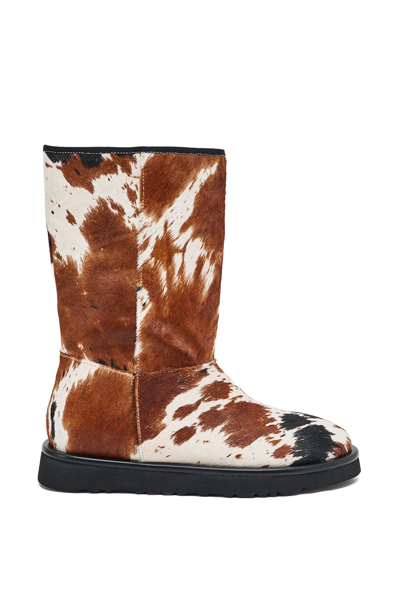 The AZALEA WANG MARLEIGH COW FLAT BOOTIE is a mid-calf bootie with a brown and white cow print genuine calf hair exterior, a soft textured finish, rounded toe, and black flat sole. 3