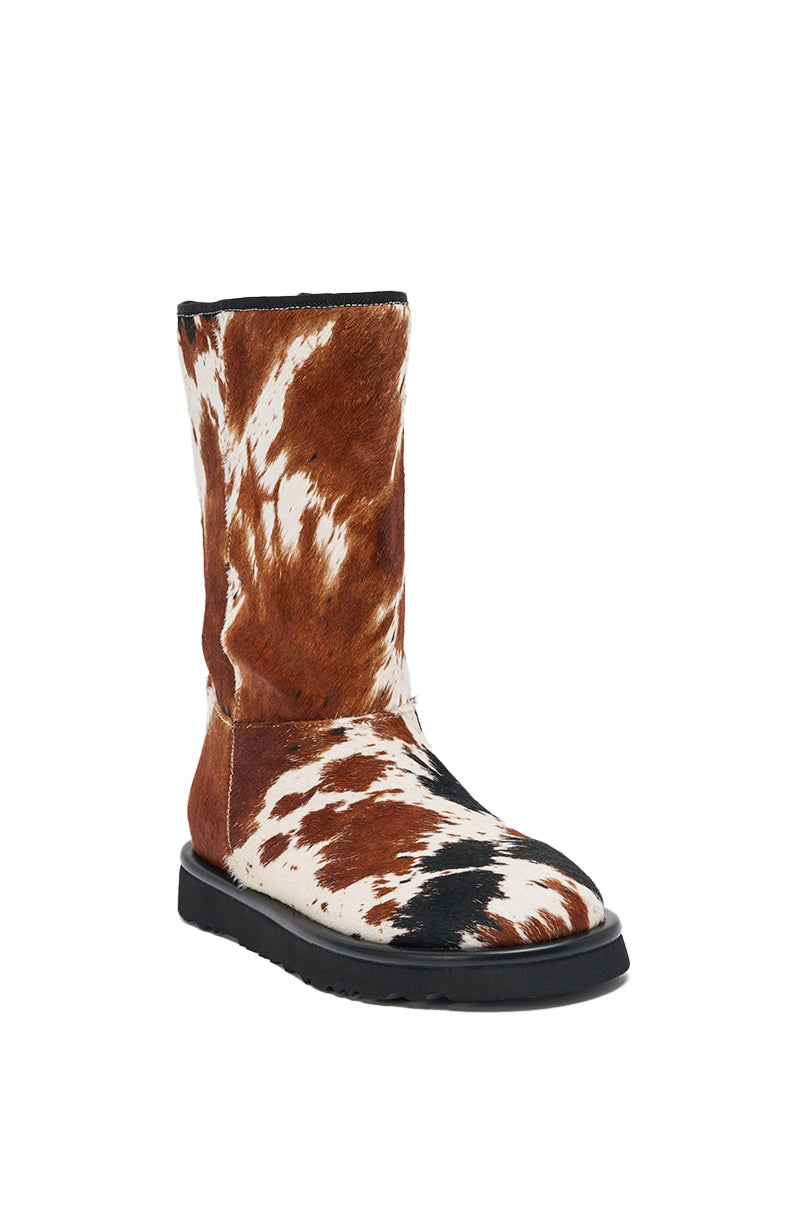 The AZALEA WANG MARLEIGH COW FLAT BOOTIE features genuine calf hair in a brown and white cow print, a flat black sole, and a mid-calf silhouette, showcased against a plain white background. 4