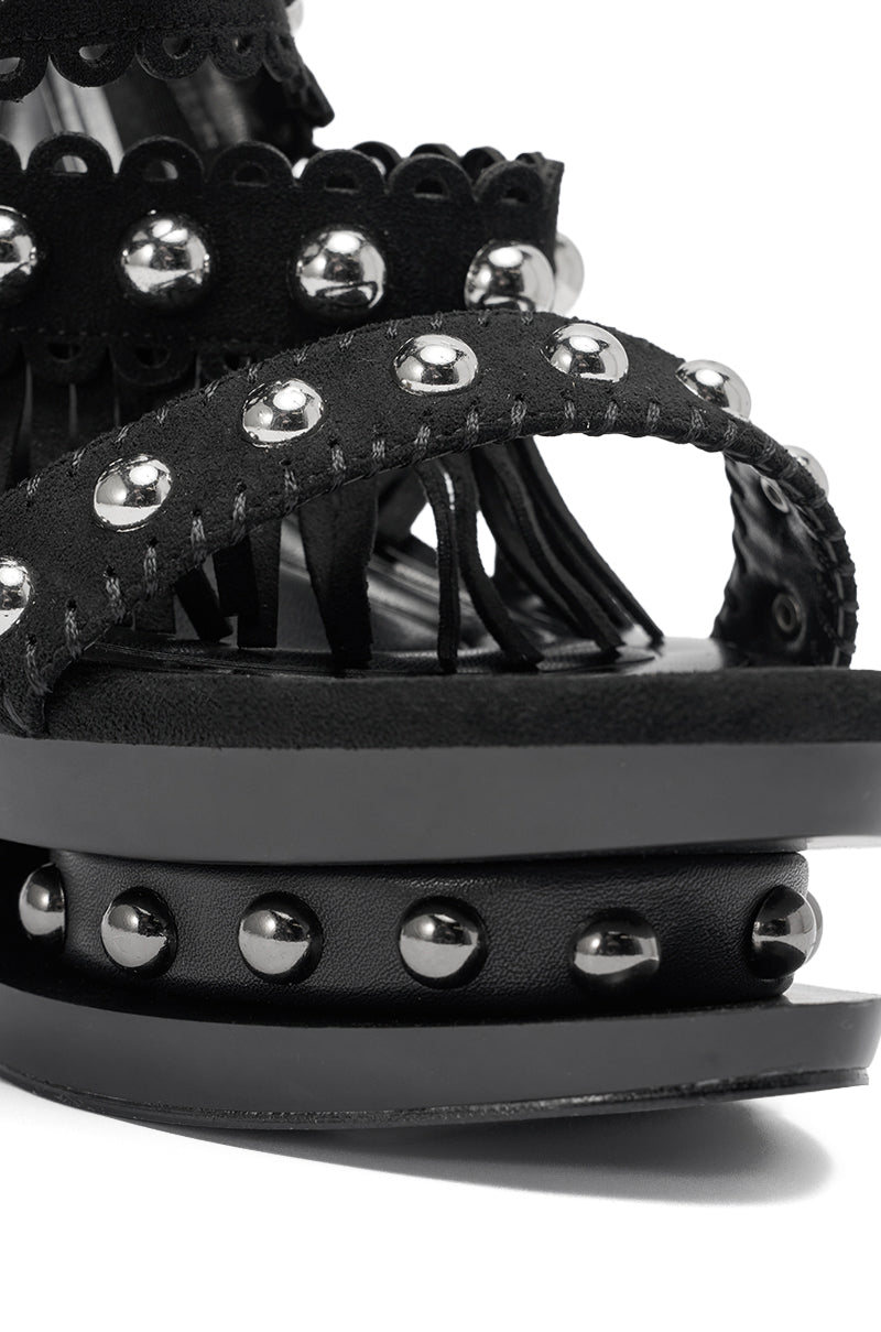 Close-up of the AKIRA GOLD MAROVA Black Novelty Platform Fringe Embellished Sandal, featuring faux suede, multiple studded straps, layered soles, and metallic studs around the base. 6