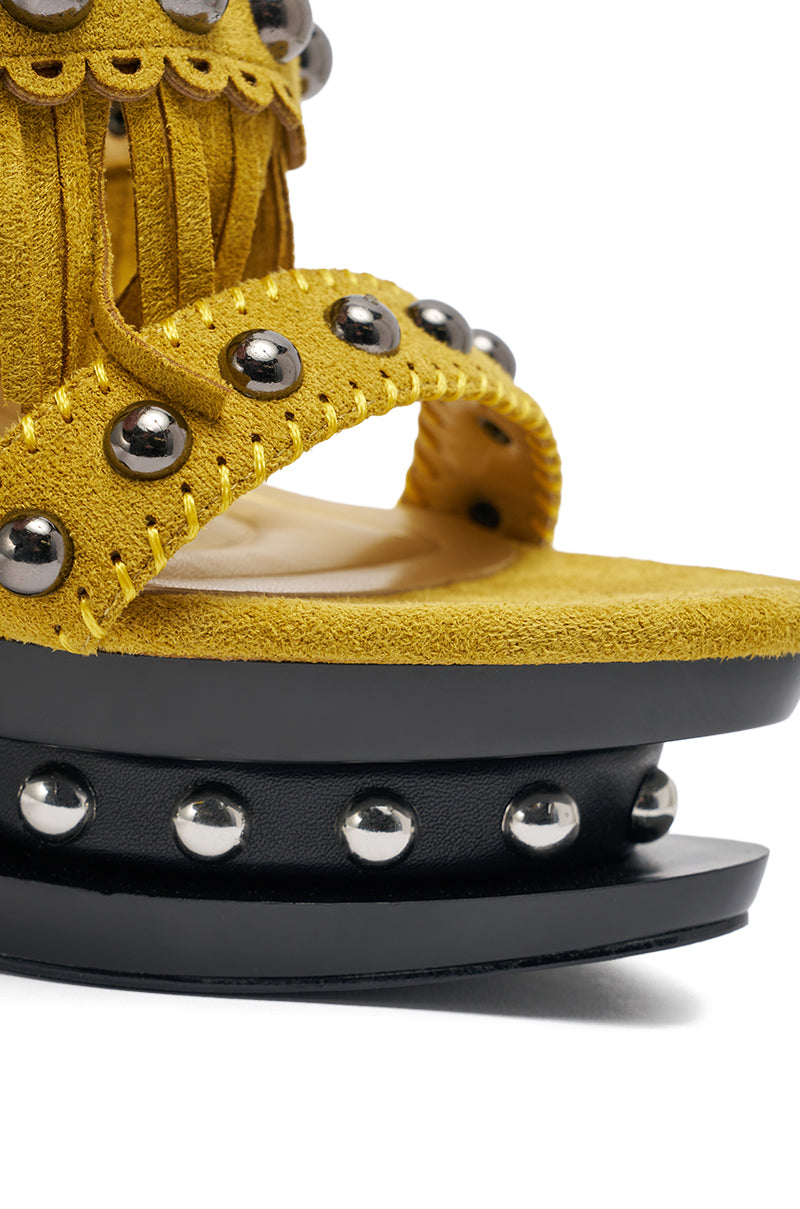 Close-up of the AKIRA GOLD MAROVA MUSTARD NOVELTY PLATFORM FRINGE EMBELLISHED SANDAL: a yellow suede platform heel with silver studs, fringe accents, and a thick black sole also detailed with silver studs. 6