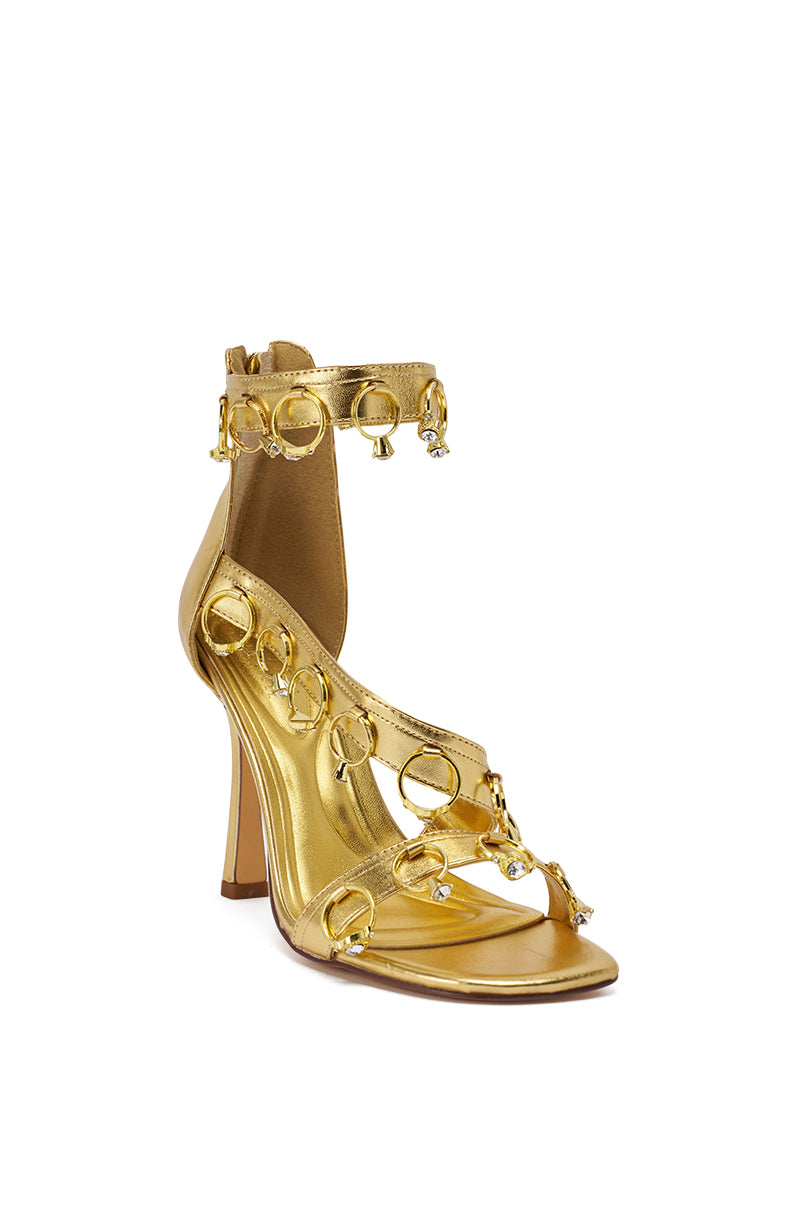 The AKIRA GOLD MARQUISE Gold Stiletto Sandal With Rings features metallic faux leather, multiple straps with circular gold rings, and small crystal accents, shown against a white background. 7