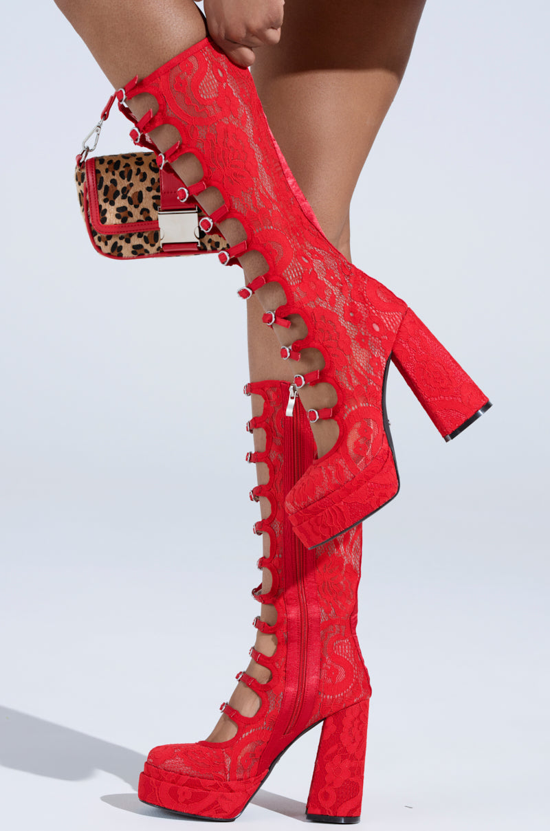 A close-up shows the AZALEA WANG MARRIGOLD BOOT IN RED LACE with chunky high heels and unique side cut-outs, paired with a leopard print handbag strapped to the mid-calf shaft against a plain white background.