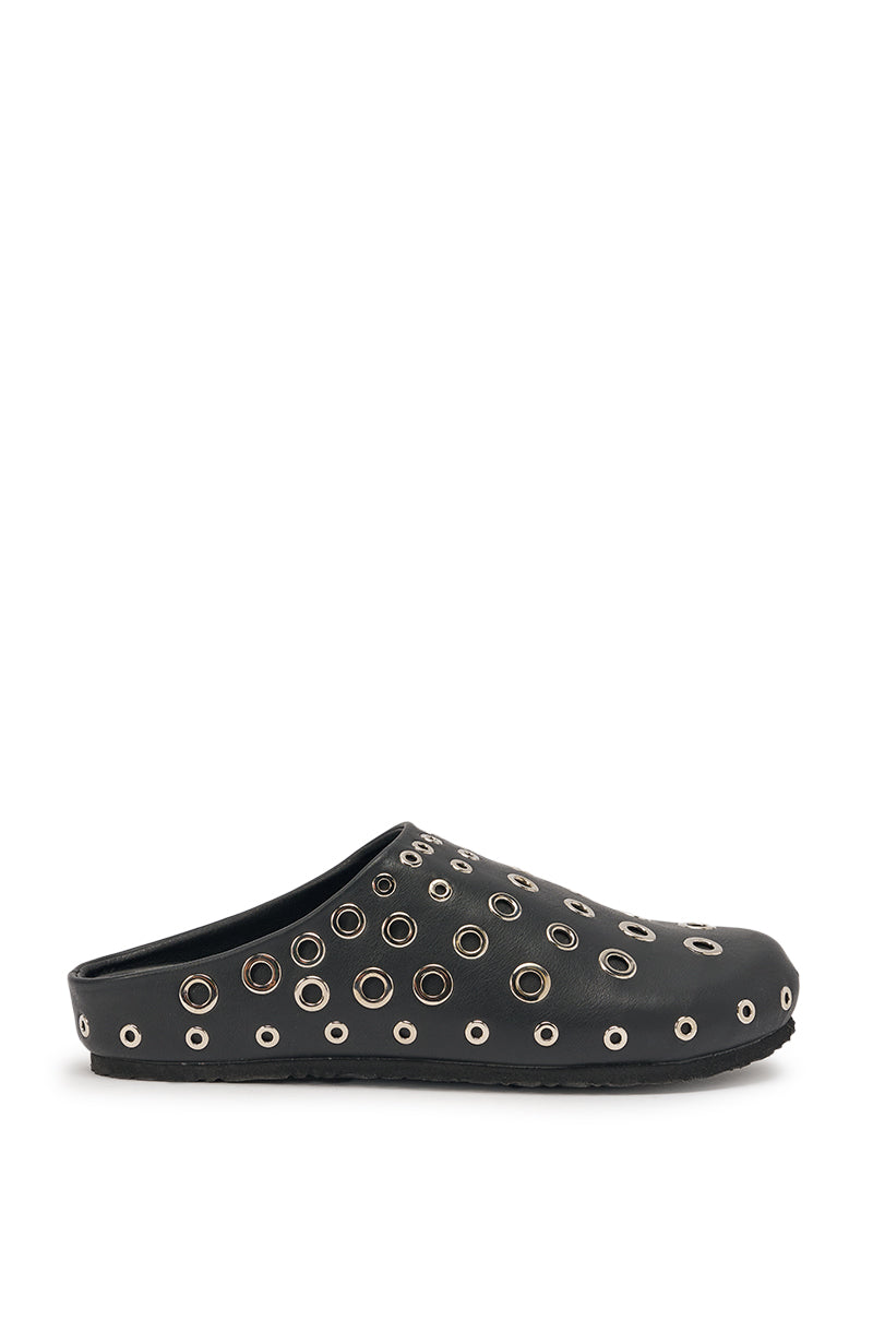 The AZALEA WANG MARSHA BLACK GROMMET DETAIL FLAT is a black faux leather slip-on clog with a closed toe, featuring multiple metal eyelets on the upper and sides, displayed against a white background. 3