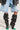 A person sports the AZALEA WANG MARVELED BLACK BOOT, which is a slouchy thigh-high boot featuring green pointed toes and stiletto heels. The boots are styled with ripped, light-wash denim shorts, and paired with a black jacket that has partially visible faux leather accents.