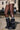 A person stands on a city sidewalk in camouflage shorts, black and white striped socks, and AZALEA WANG MATE BLACK RUCHED BOOTS with a flatform sole; parked cars and a beige brick building are visible in the background.