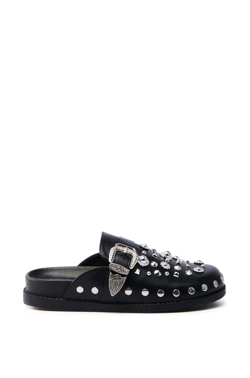 The AZALEA WANG MAULDIN HARDWARE EMBELLISHED CLOG IN BLACK is a vegan leather slip-on mule with an almond toe, silver studs, ornate side buckle, round metallic decorations on the upper, and a flat sole, set against a white background.