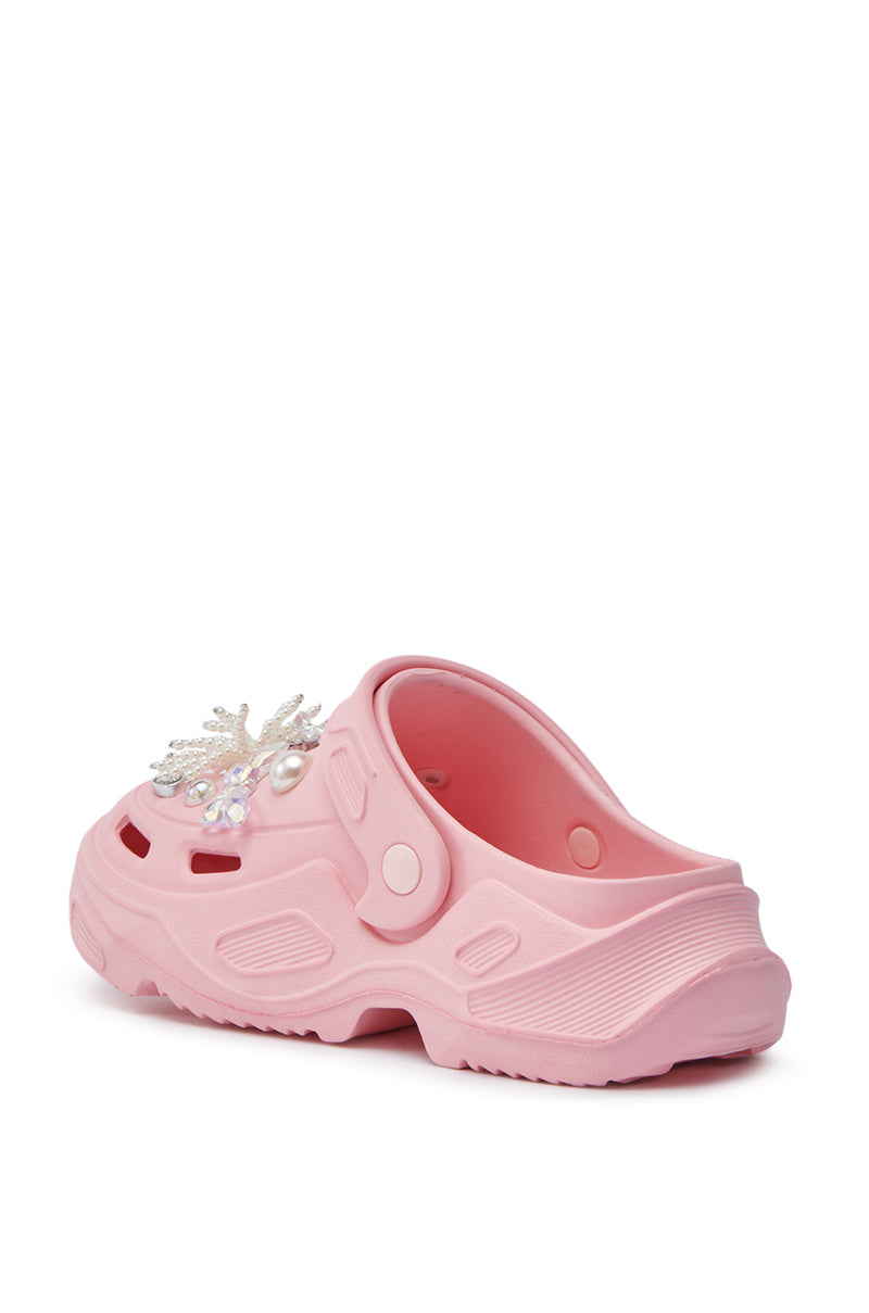 The AZALEA WANG MAVA PINK PEARL IRIDESCENT FLAT is a slip-on clog sandal with textured soles, an almond toe, jeweled snowflake charm, ventilation holes, pearl details, and an adjustable heel strap.