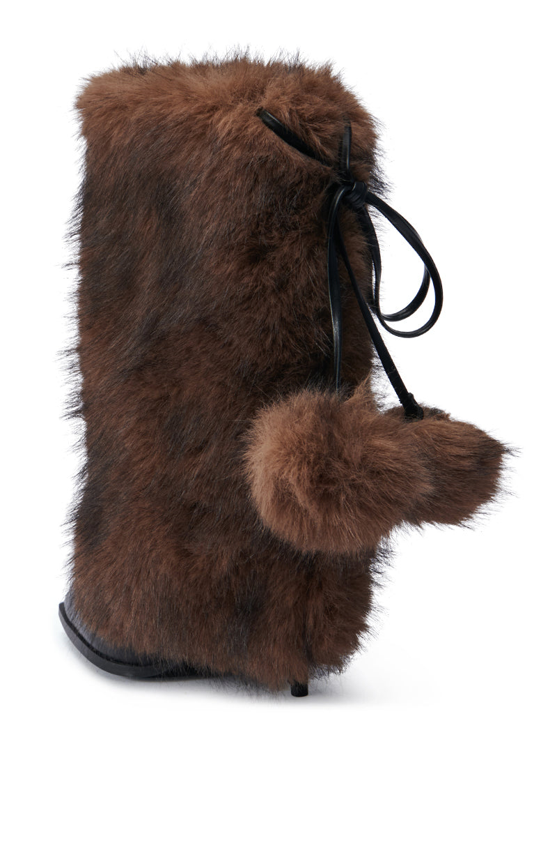 The AZALEA WANG MAYRA BROWN BOOTIE showcases a plush furry texture with a charming side pom-pom detail, elegantly tied with a black ribbon. This faux leather bootie is designed with a sleek black sole and features a mid-calf shaft, beautifully contrasted against a white background.