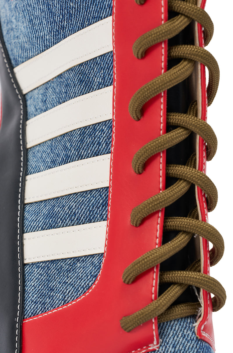 Close-up of the AKIRA GOLD MAYWEATHER MULTI SPORTY LOOK WEDGE BOOTIE featuring denim-like fabric, white stripes, red vinyl trim, black accents, and brown laces threaded through red eyelets.