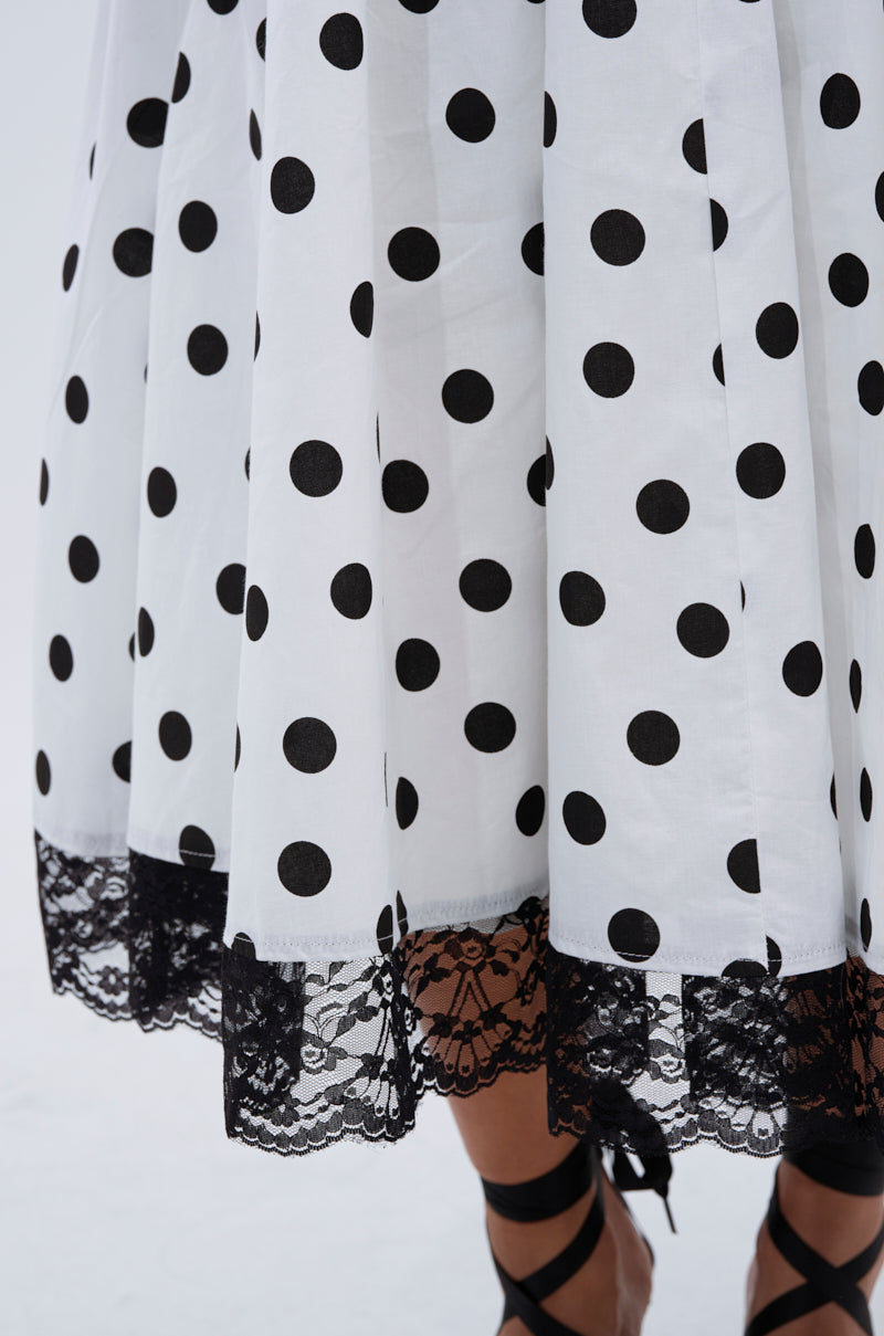 A close-up of the DOLLY POLKA DOT MIDI DRESS featuring black lace trim at the hem, styled with black ribbon-tied shoes below.