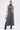 A woman models the DONT GIVE UP MOCK NECK KNIT MAXI DRESS—featuring a mock neck, flared hem, and body-contouring seams—with black boots and a metallic handbag, posed against a plain white background.