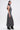 A woman in profile wears the DONT GIVE UP MOCK NECK KNIT MAXI DRESS with body-contouring seams, a flared hem, and black boots. Her long dark hair is half-up in a ponytail, set against a plain light background.