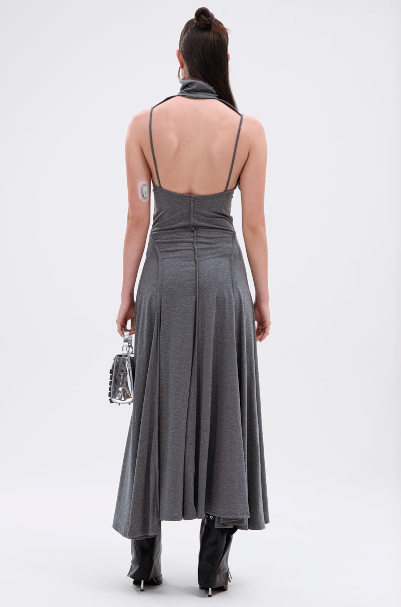 A woman faces away wearing the DONT GIVE UP MOCK NECK KNIT MAXI DRESS, a gray, body-contouring maxi with thin straps. She carries a small silver handbag, wears black heeled boots, and has an insulin patch on her upper left arm.
