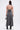 A woman faces away wearing the DONT GIVE UP MOCK NECK KNIT MAXI DRESS, a gray, body-contouring maxi with thin straps. She carries a small silver handbag, wears black heeled boots, and has an insulin patch on her upper left arm.