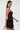 A woman with long dark hair models the DORELLA LACE MINI DRESS, featuring a skater silhouette, against a white background. She accessorizes with hoop earrings and holds a black circular handle while looking over her shoulder.